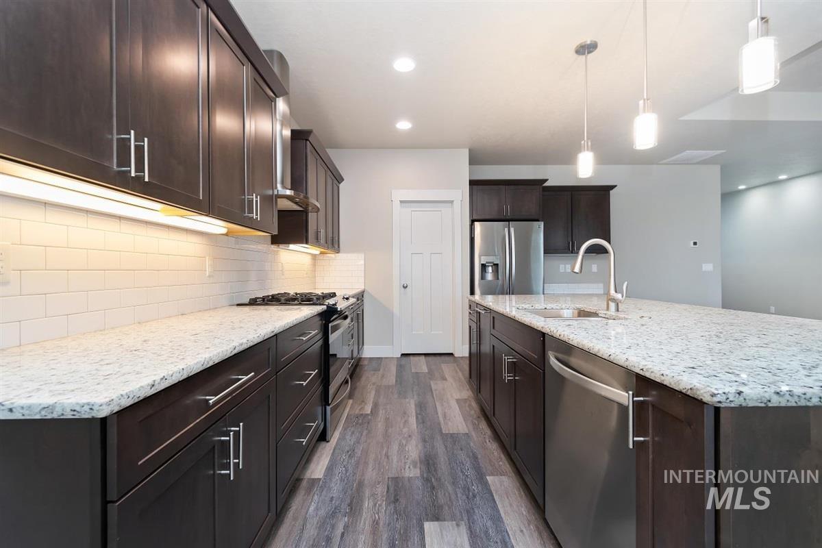 9580 West Ringle Creek Street Star, ID 83669 - Photo 18 of 43 Kitchen with dark wood finish cabinetry, stainless steel appliances, light stone countertops, dark wood-type flooring, and an island with sink