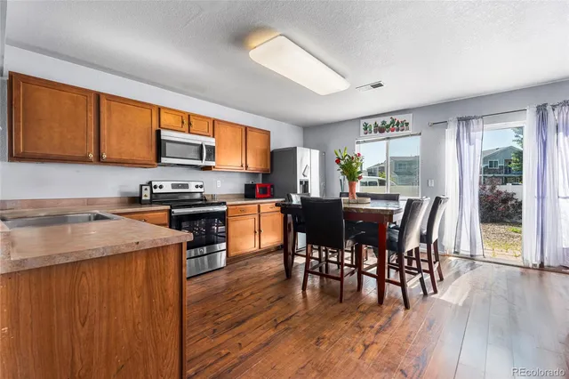 a open kitchen with stainless steel appliances granite countertop a stove top oven a sink a dining table and chairs with wooden floor