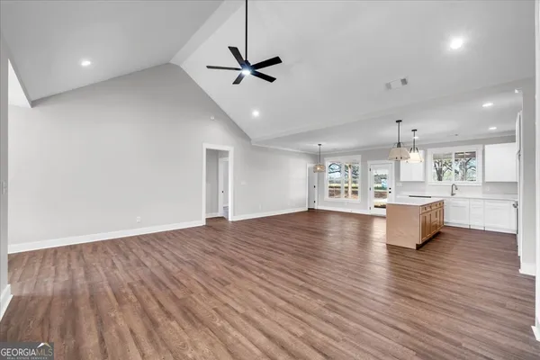 a view of an empty room and kitchen with wooden floor