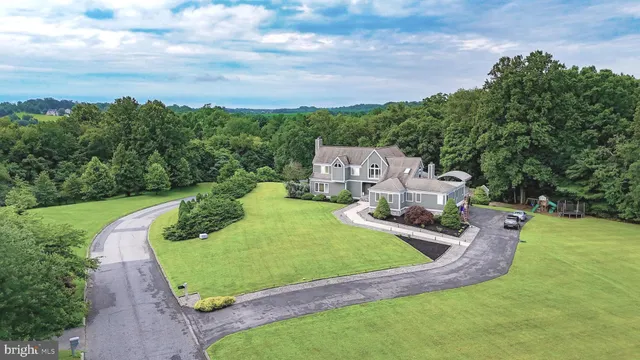 a house that is sitting in the grass with large trees and plants