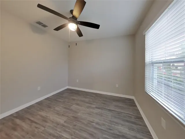 an empty room with wooden floor fan and windows