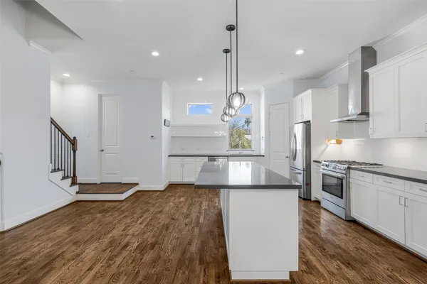 a kitchen with kitchen island a counter top space a stove a refrigerator cabinets and wooden floor