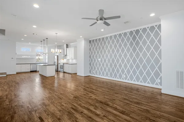 a view of an empty room and kitchen with wooden floor