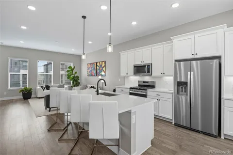 a kitchen with stainless steel appliances granite countertop a refrigerator a stove a sink a dining table and chairs with wooden floor