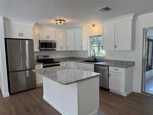 a kitchen with kitchen island granite countertop a sink cabinets and stainless steel appliances