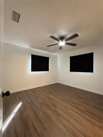 a view of an empty room with wooden floor and a ceiling fan