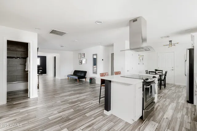 a kitchen with stainless steel appliances a stove top oven a sink dishwasher a refrigerator white cabinets and wooden floor