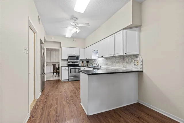 a kitchen with stainless steel appliances granite countertop a refrigerator a sink dishwasher a stove and white countertops with wooden floor