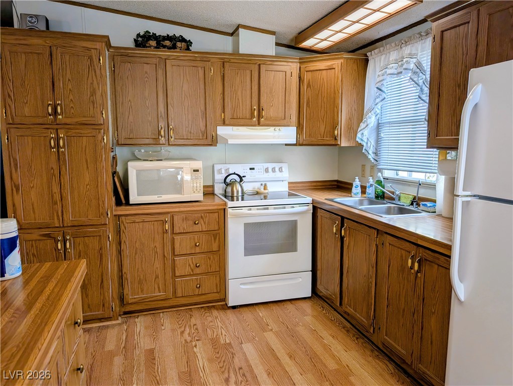 50 North 2nd Street Panaca, NV 89042 - Photo 12 of 35 Kitchen featuring white appliances, brown cabinetry, light wood-style floors, ornamental molding, and a textured ceiling