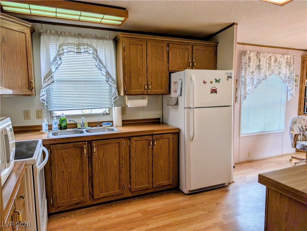 50 North 2nd Street Panaca, NV 89042 - Photo 13 of 35 Kitchen with white appliances, light wood-style floors, brown cabinets, and a textured ceiling
