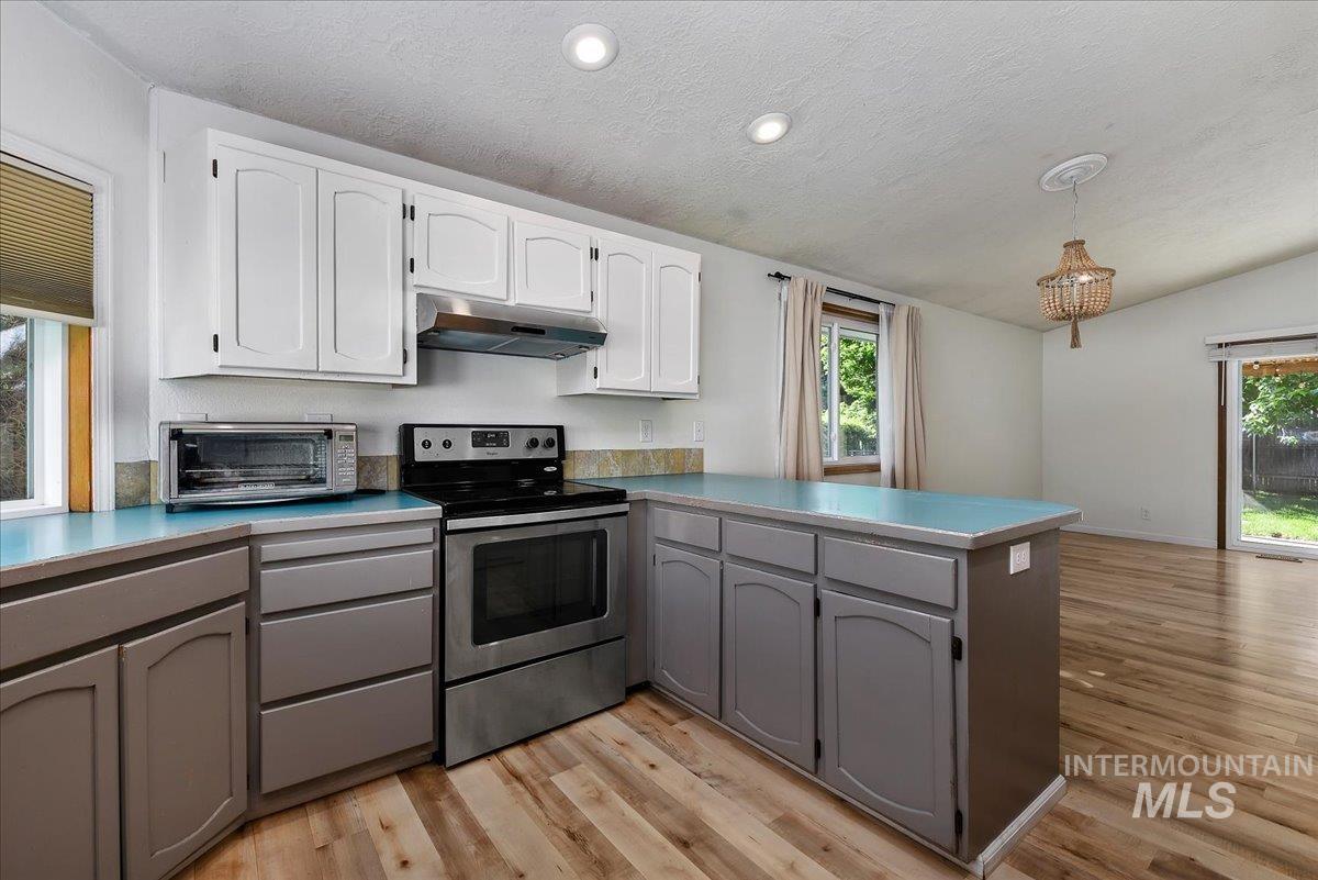 9215 West Preece Street Boise, ID 83704 - Photo 5 of 22 Kitchen featuring white upper cabinetry, gray lower cabinetry, and a stainless steel electric range with an overhead vent hood