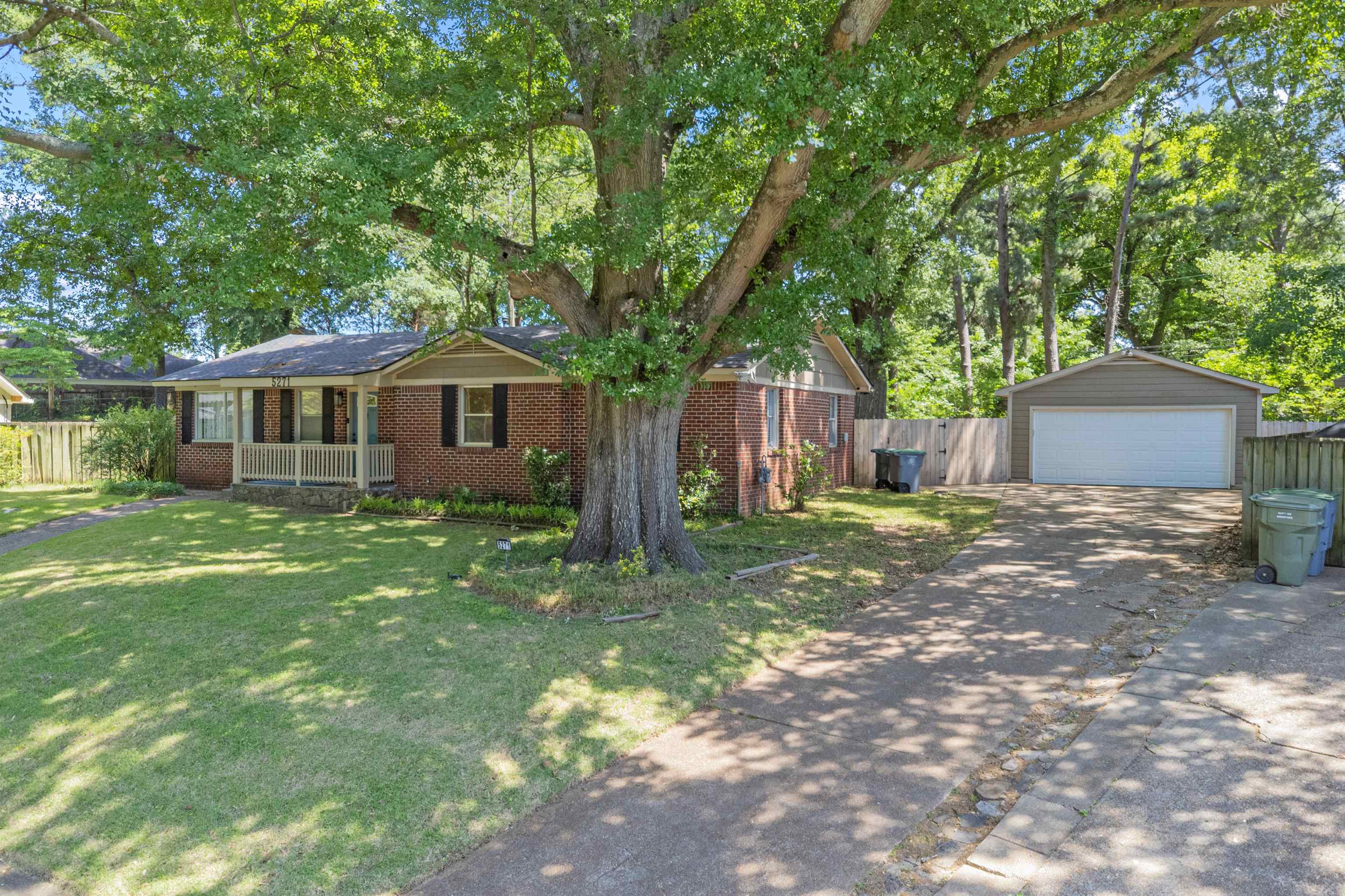 5271 Princeton Road Memphis, TN 38120 - Photo 2 of 30 Brick facade property featuring a prominent mature tree, front porch with white railing, and a detached two-car garage