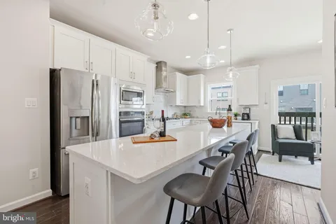 a kitchen with stainless steel appliances a refrigerator a stove a sink a dining table and chairs with wooden floor