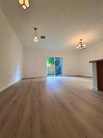 an empty room with wooden floor chandelier fan and windows