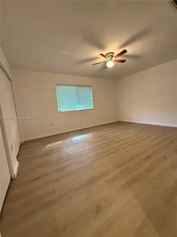 an empty room with wooden floor ceiling fan and windows