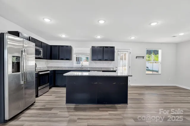 a kitchen with stainless steel appliances kitchen island granite countertop a refrigerator a sink dishwasher a stove and a microwave oven with wooden floor