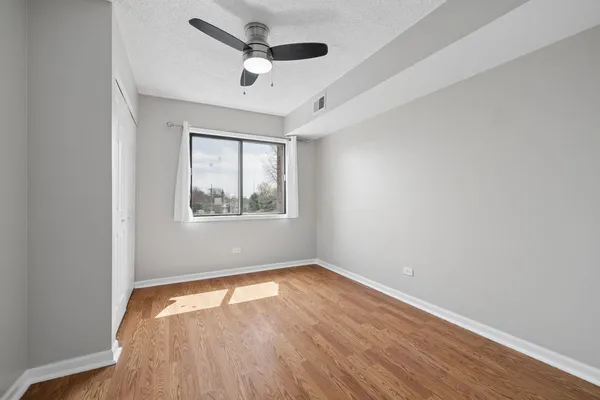an empty room with wooden floor ceiling fan and windows