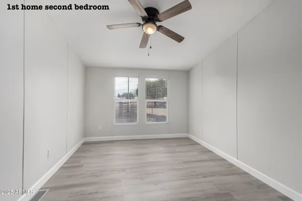 an empty room with wooden floor ceiling fan and windows