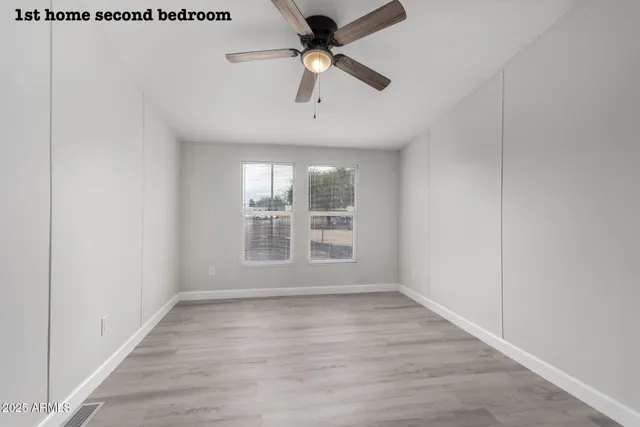 an empty room with wooden floor ceiling fan and windows