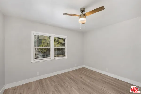 an empty room with wooden floor ceiling fan and windows