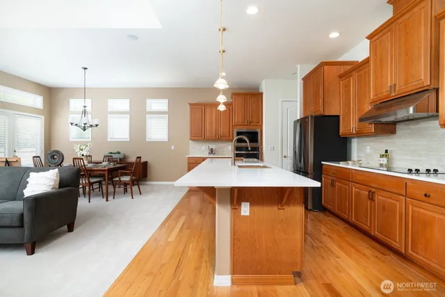 a large kitchen with stainless steel appliances kitchen island granite countertop a refrigerator a stove a sink a dining table and chairs with wooden floor