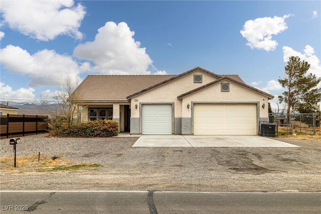 Ranch-style house featuring fence, a tiled roof, an attached garage, concrete driveway, and stucco siding