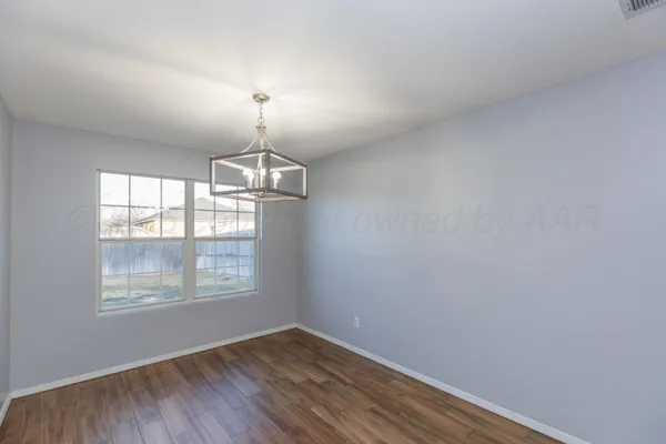 an empty room with wooden floor chandelier and windows