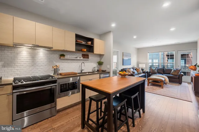 a kitchen with stainless steel appliances a stove a sink a refrigerator white cabinets and couches with wooden floor