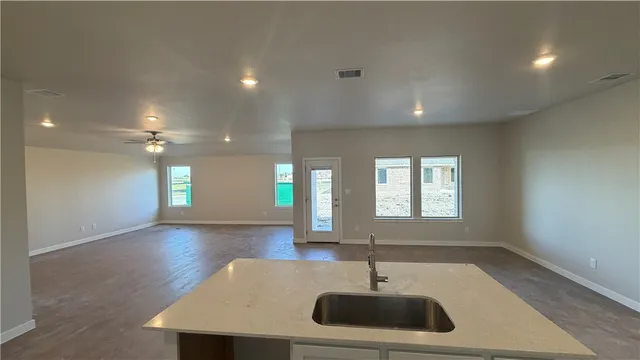 an empty room with wooden floor chandelier fan and windows