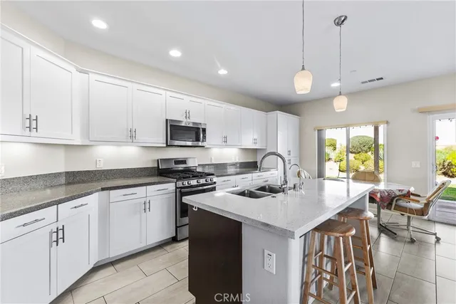 a kitchen with stainless steel appliances granite countertop a sink a stove a refrigerator and white cabinets with wooden floor