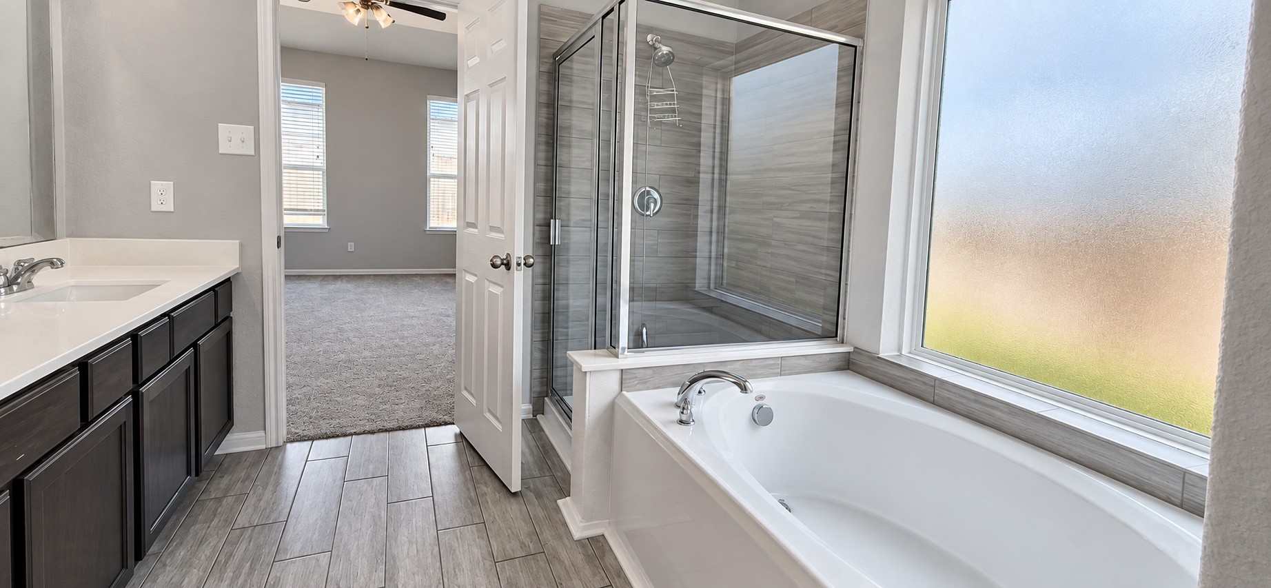 11355 Cascading Stream Way Houston, TX 77044 - Photo 10 of 17 Experience luxury in this elegant bathroom featuring a spacious soaking tub, sleek glass-enclosed shower, and dual vanity sinks with modern fixtures, all bathed in natural light from large windows.