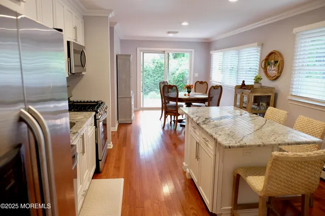 a open kitchen with stainless steel appliances granite countertop a stove a refrigerator a dining table and chairs with wooden floor