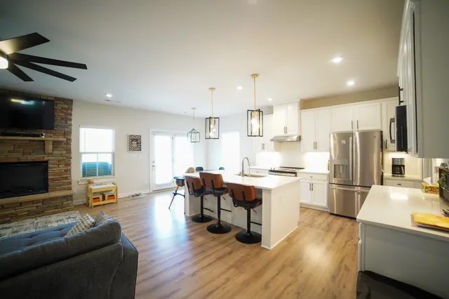 a living room with stainless steel appliances furniture a fireplace a flat screen tv and wooden floor