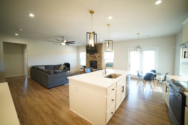 a large living room with stainless steel appliances granite countertop a sink dishwasher a stove a dining table and chairs with wooden floor