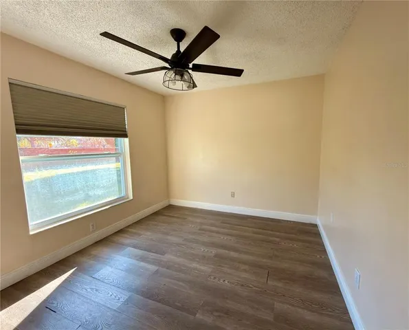 an empty room with wooden floor fan and windows