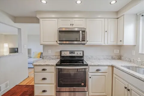 a kitchen with granite countertop white cabinets and a stove top oven