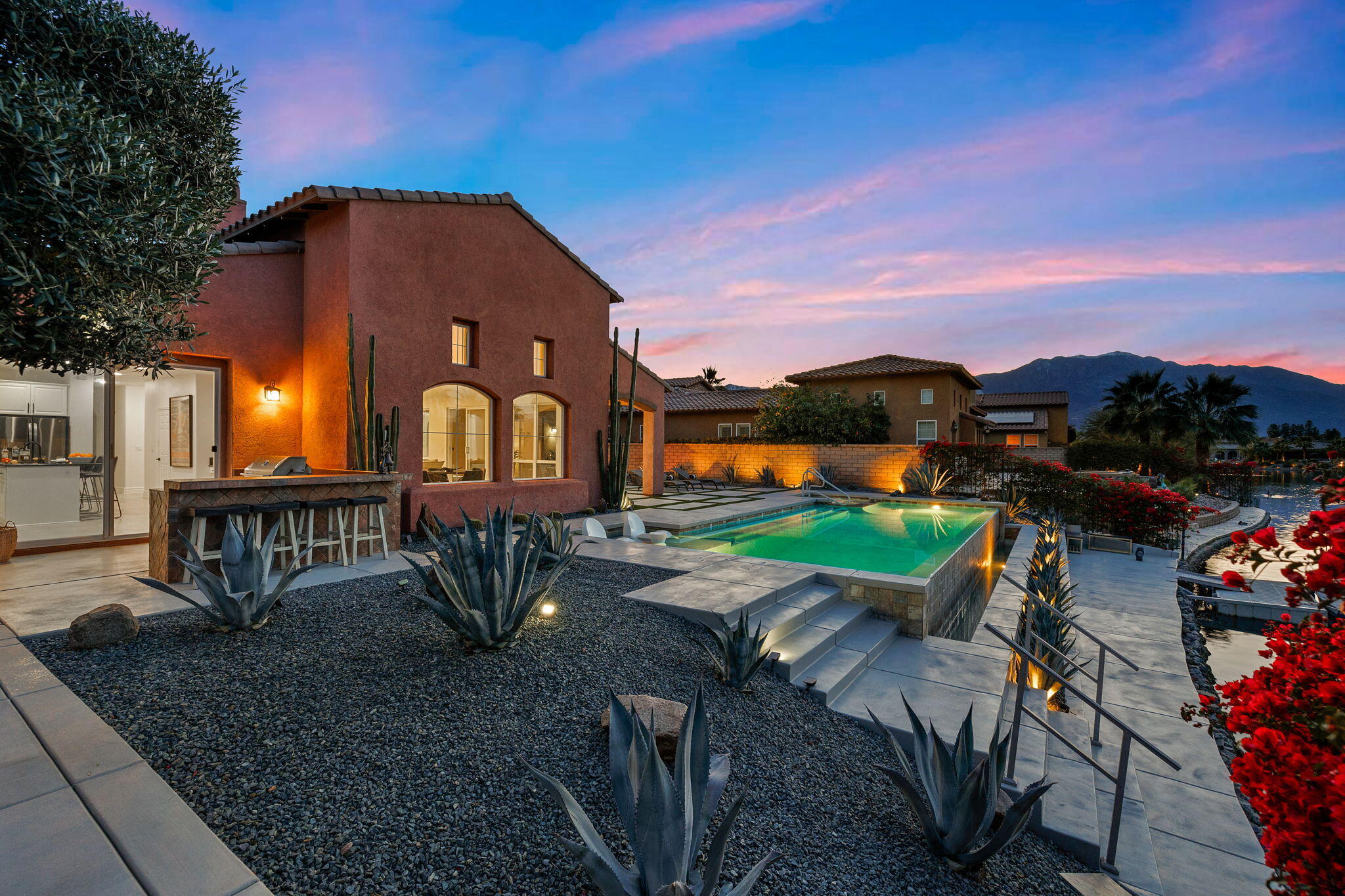 6 Via Santa Ramona Rancho Mirage, CA 92270 - Photo 38 of 60 a view of a brick house with a yard and table and chairs under an umbrella