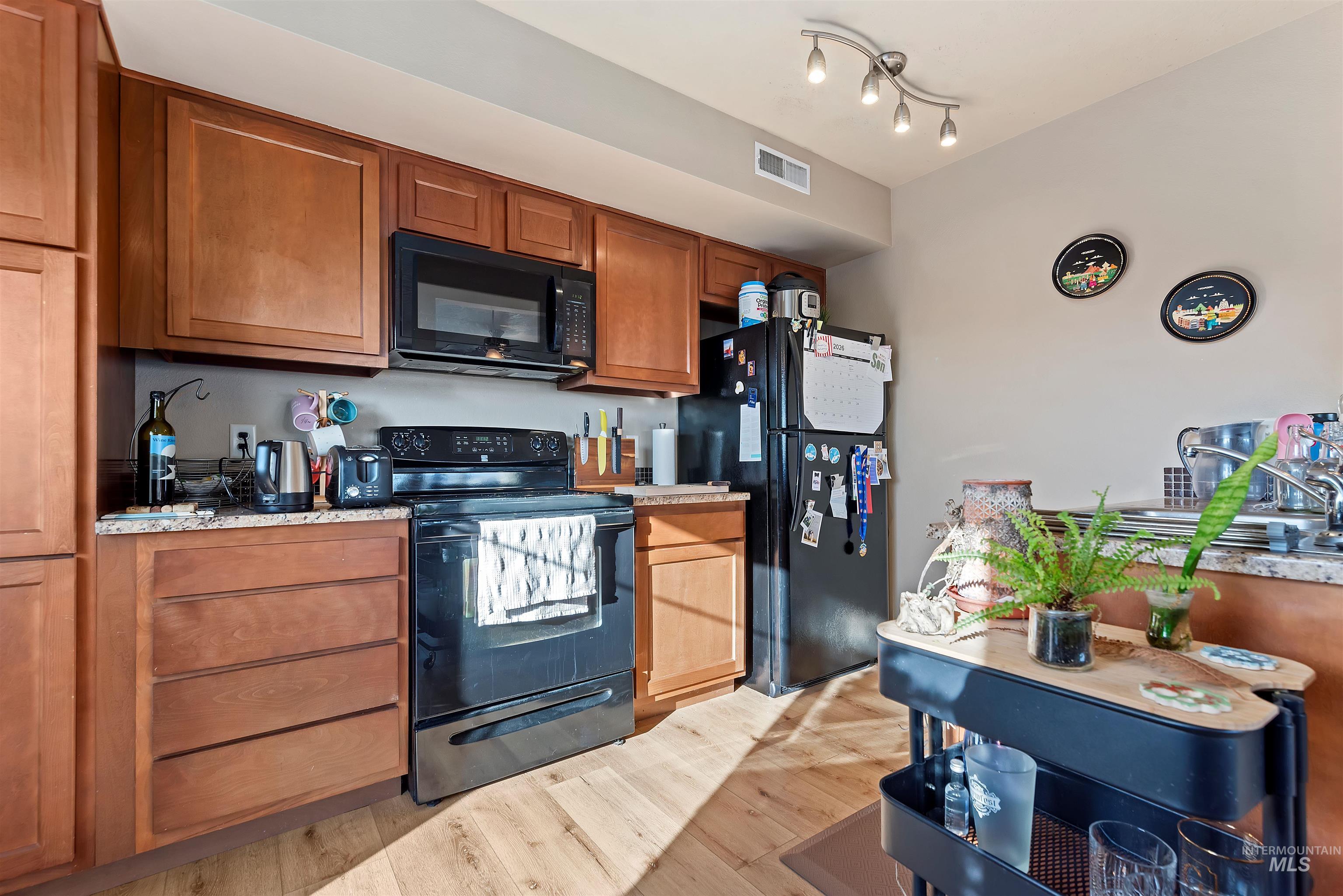 9107 Ustick Road Boise, ID 83704 - Photo 6 of 8 Kitchen with black appliances, wood finish cabinets, light wood finished floors, and light stone counters