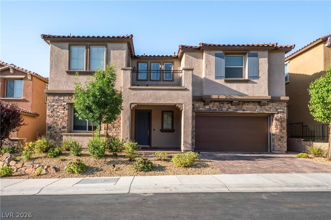 Two-story home with a tiled roof, stucco siding, and stone accents boasts a second-story balcony and an integrated garage.