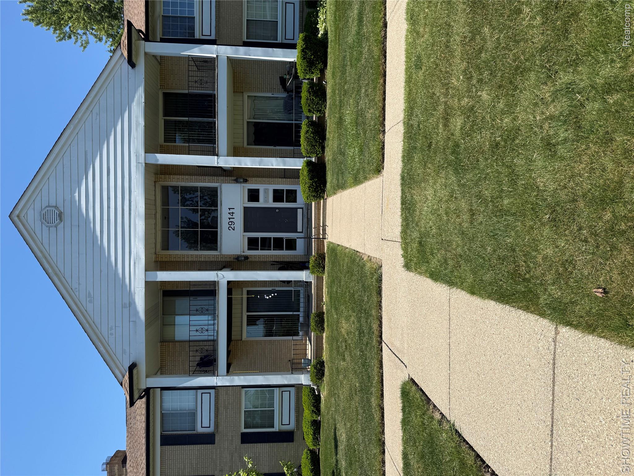 Brick exterior with white column accents, multiple private balconies with black railings, and a central entrance featuring large windows