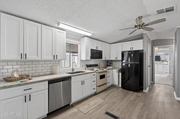 a kitchen with stainless steel appliances granite countertop a refrigerator a sink dishwasher a stove top oven a refrigerator with white cabinets and wooden floor