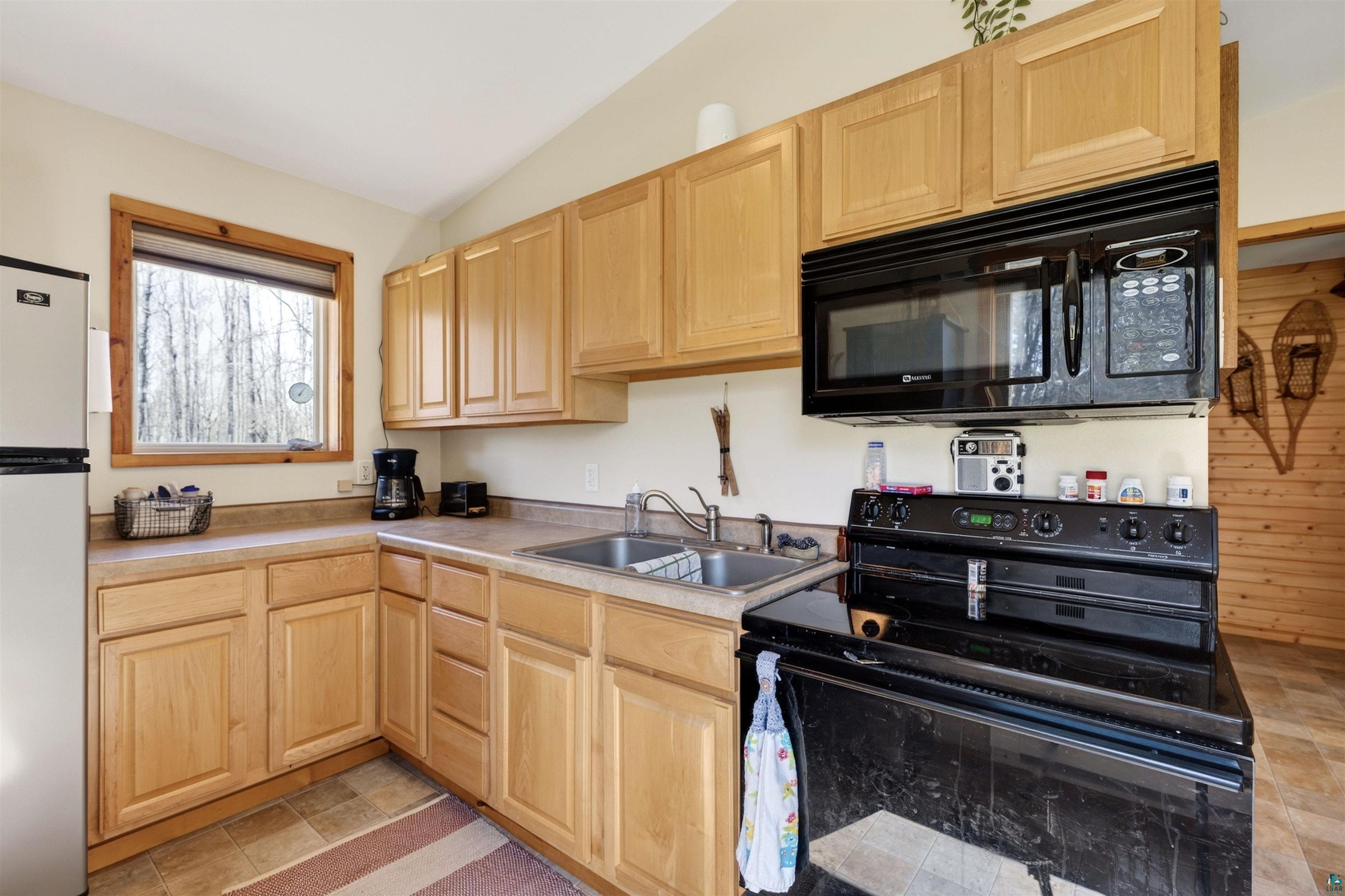 12235 East Crooked Lake Road Gordon, WI 54838 - Photo 17 of 48 Kitchen featuring wood-finish cabinetry, a stainless steel double sink, a black range with an overhead microwave, and a window with a wood-trimmed frame