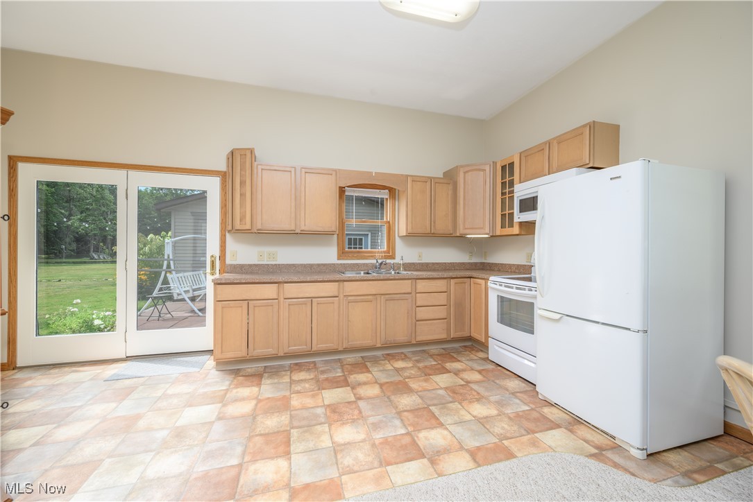 6640 Giddings Road Rootstown, OH 44272 - Photo 45 of 49 Kitchen featuring white appliances, light brown cabinets, light countertops, glass insert cabinets, and stone finish flooring