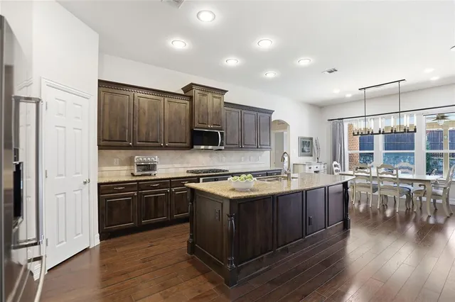 a kitchen with granite countertop a stove a sink a dining table and chairs with wooden floor