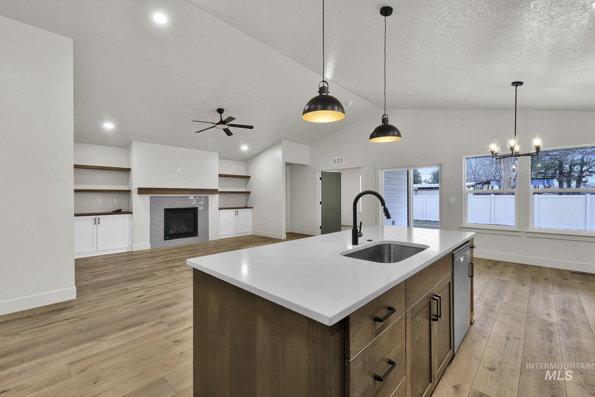 1130 Velvet Loop Wilder, ID 83676 - Photo 15 of 35 Open-concept living area featuring a kitchen island with integrated sink, wood-finish flooring, a vaulted ceiling, a fireplace with tile surround, and built-in shelving