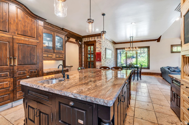 811 South High Ridge Drive Alpine, UT 84004 - Photo 20 of 98 Kitchen featuring glass fronted cabinets, a center island with sink, ornamental molding, light stone counters, and stone tile flooring