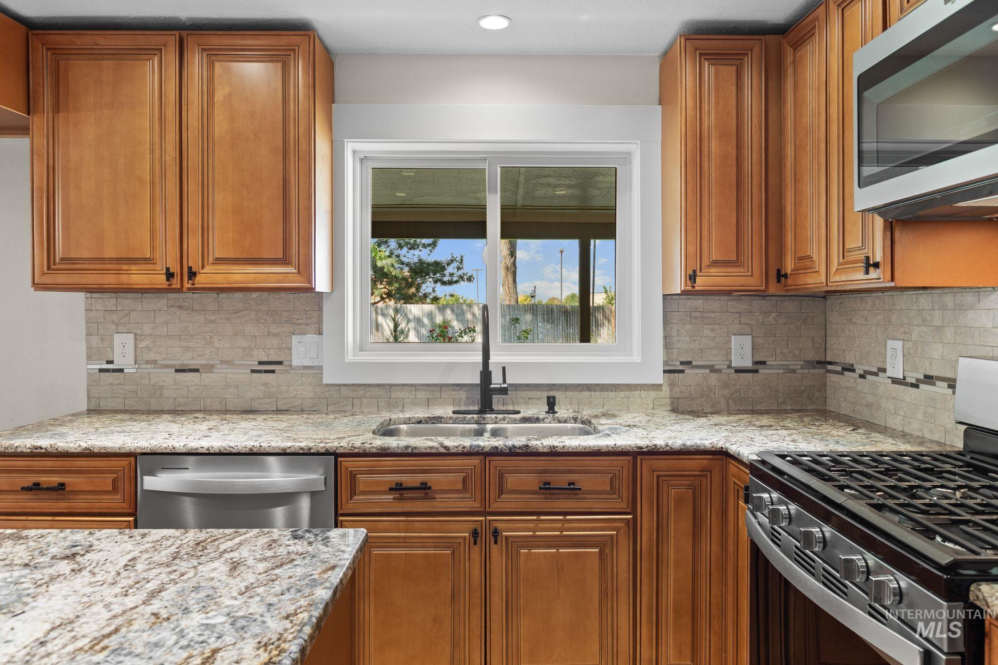 1675 Country Terrace Way Meridian, ID 83642 - Photo 12 of 50 Wood-finish cabinetry, stone countertops, stainless steel appliances, tile backsplash, and a stainless steel sink with a black-finish faucet