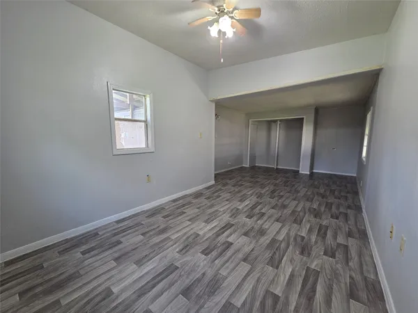 a view of an empty room with wooden floor and a chandelier fan