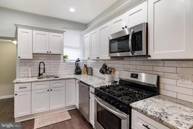 a kitchen with stainless steel appliances white cabinets granite counter tops and a window