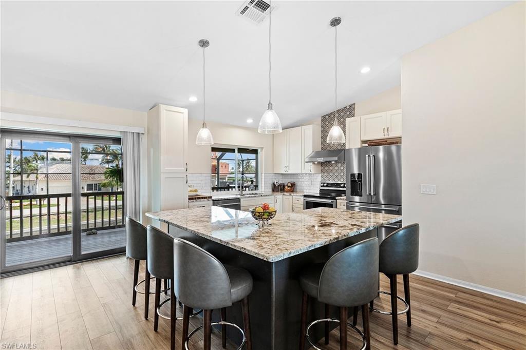 21531 Madera Road Fort Myers Beach, FL 33931 - Photo 7 of 49 a open kitchen with stainless steel appliances granite countertop a stove a refrigerator a kitchen island with a dining table and chairs